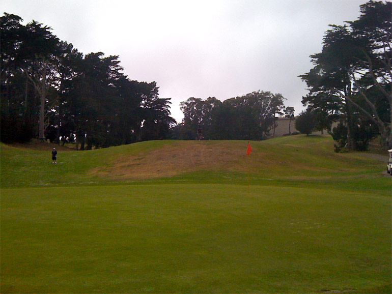 From behind the green, note the size of the 11th hole's mound relative to the size of the golfers on and to the left of it.