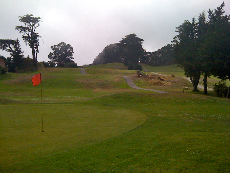 The 8th green in the foreground, 7th fairway upper-middle, and 9th fairway going uphill towards the trees top-right.