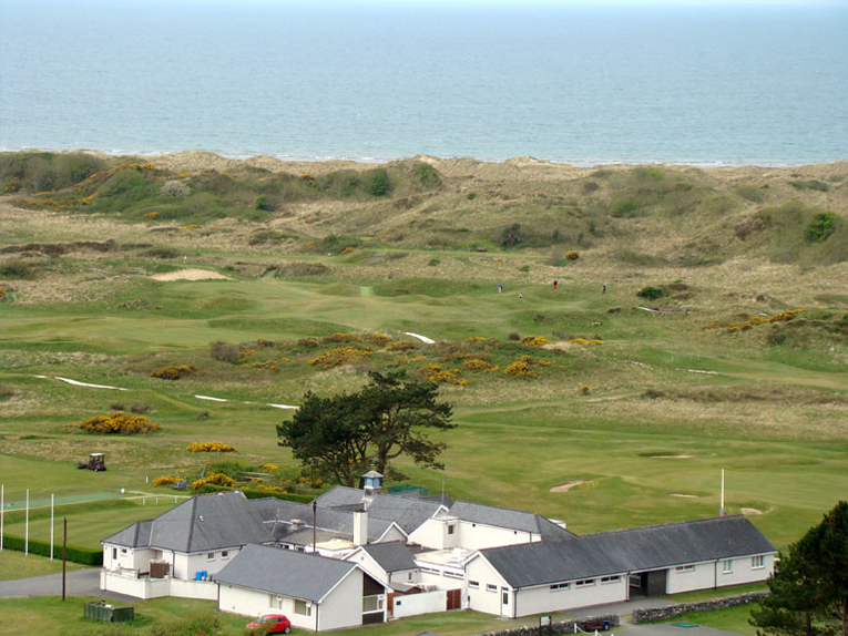 As seen from Harlech Castle, Royal St. David’s clubhouse is in the foreground followed by its scintillating closing stretch of holes in the dunes. The golfer in red battles down the roly-poly fourteenth.