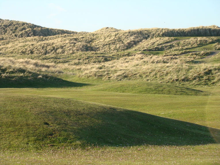 This view from across the course of the fourteenth tee areas benched into dune gives a sense of how much the fourteenth falls from tee to green. Controlling one's tee ball from a perched tee is never easy in a windy environment like Scotland.